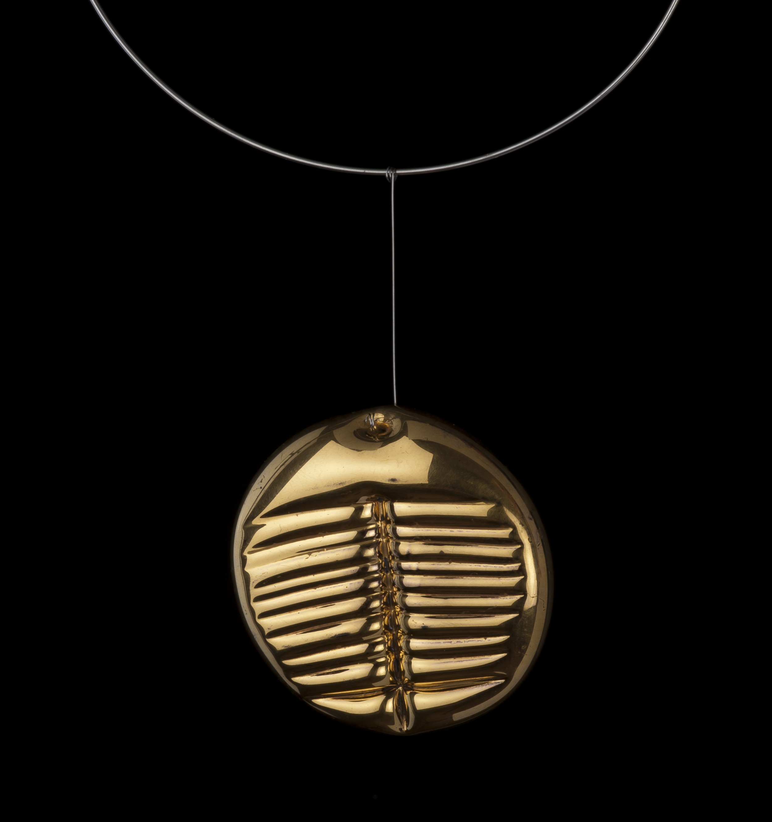 Obr-38: Lubomír Blecha, šperk „Trilobit“, hutně tvarovaný sklený šperk, čelně zlacený, inversní plocha zabroušená a zaleštěná, ?6,2 cm, 1980, vznikl z podnětu společných studii „znaků pro šlechetnou bytost“         